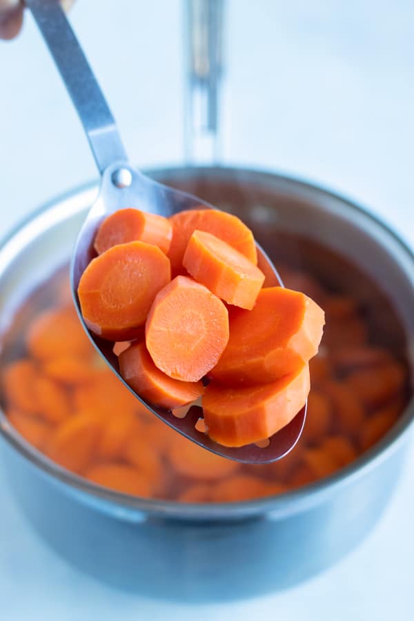 Sliced carrots are lifted from a pot of boiling water.