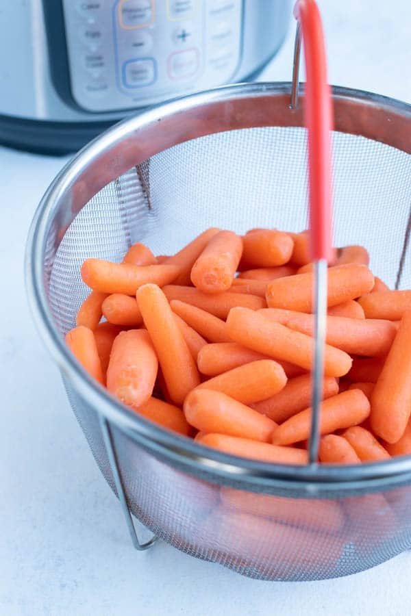 Baby carrots are placed in a strainer in the instant pot.