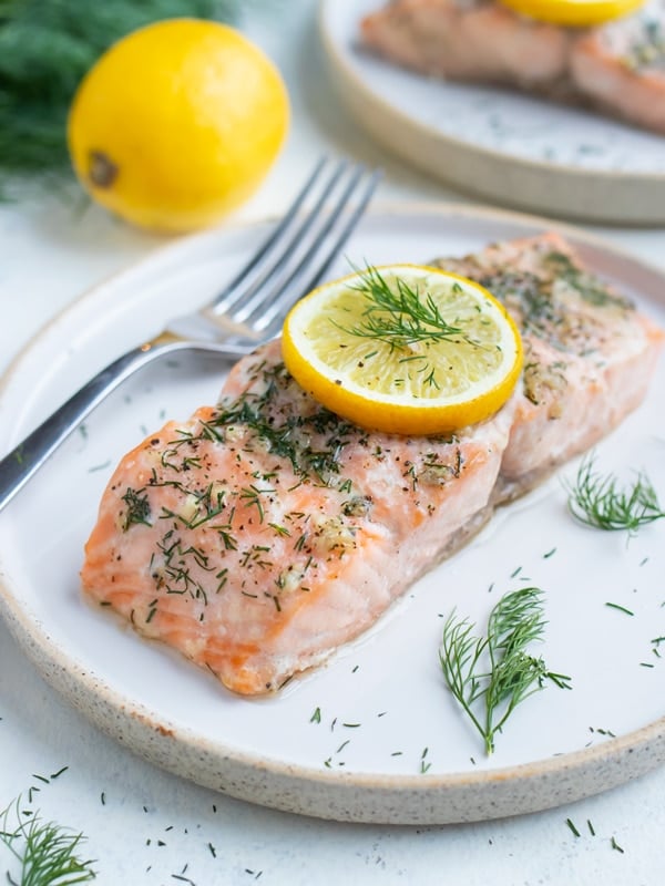 Salmon is served on a a white plate with a fork.