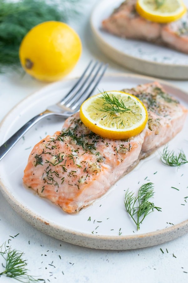 Fresh dill is placed on a plate with a healthy salmon dish.