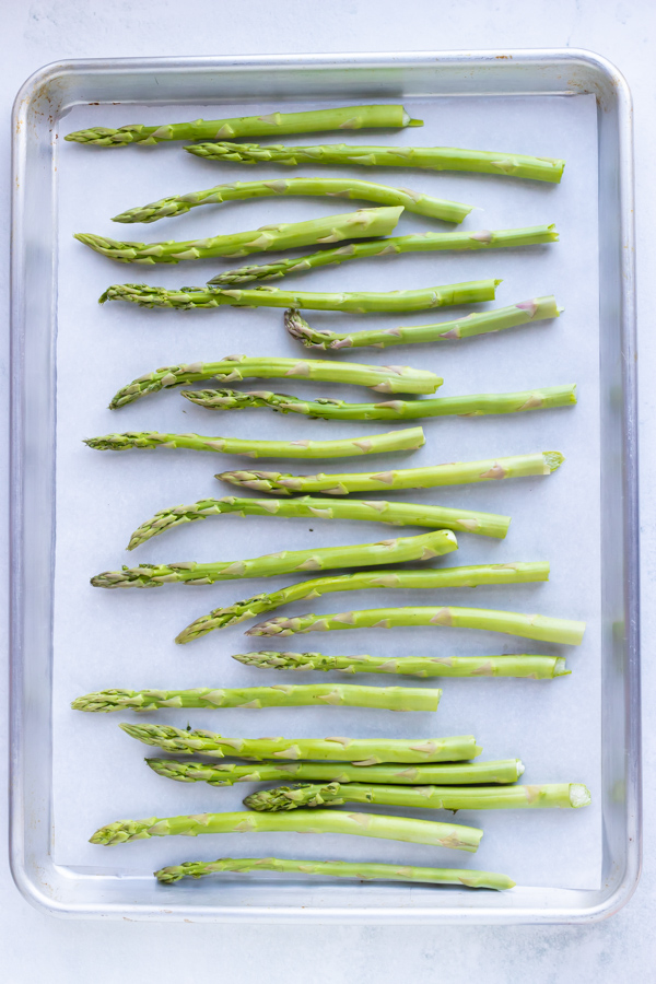 Trimmed asparagus spears in a single layer on a parchment paper lined baking sheet.