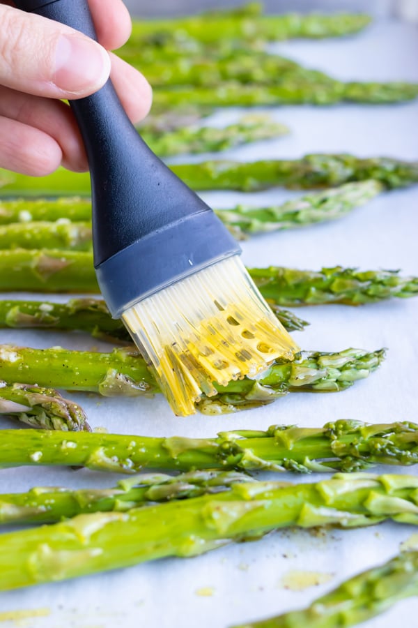 Brushing a lemon garlic sauce over asparagus spears before roasting in the oven.