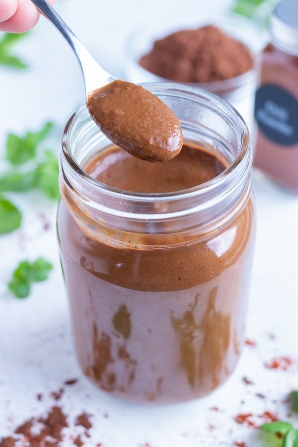 Mole sauce is lifted out of a jar with a metal spoon.