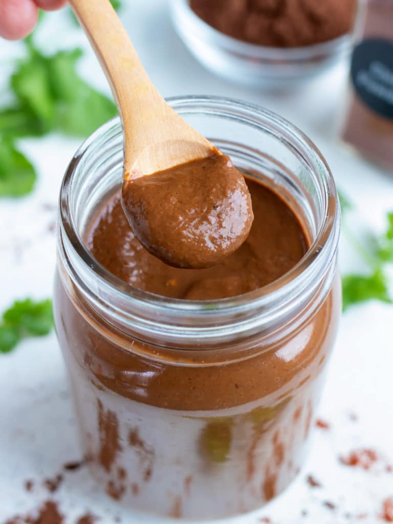 A wooden spoon is used to lift Mole sauce out of a jar.