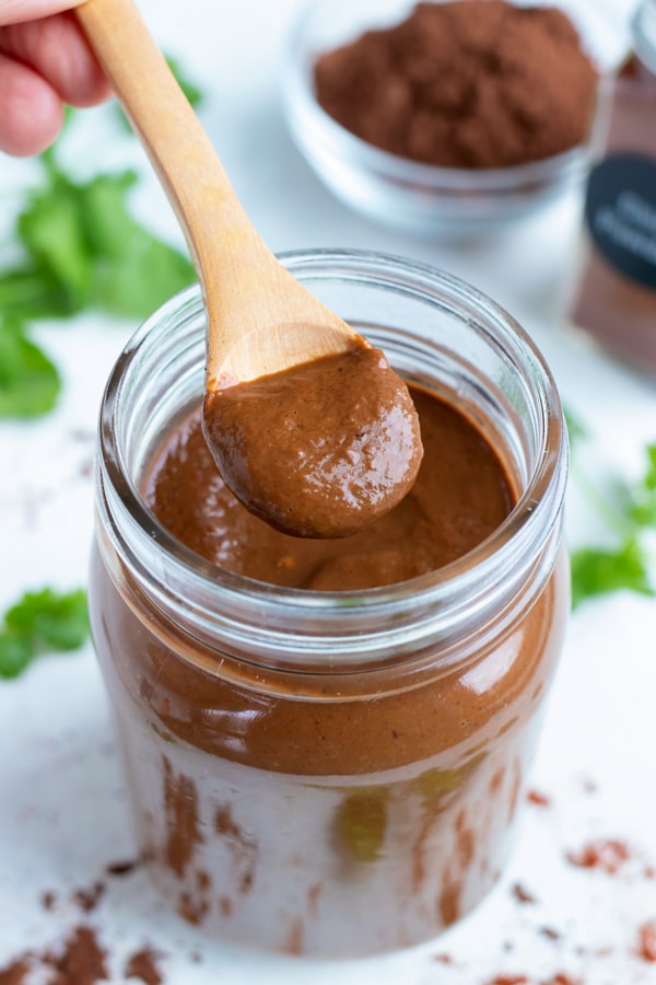 Wooden spoon is used to lift up mole sauce from a mason jar.