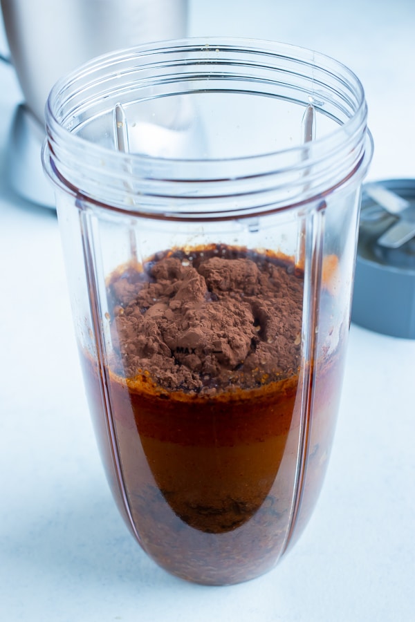 The onions, chipotle peppers, almond butter, raisins, cocoa powder, and remaining broth are added to a high speed blender.
