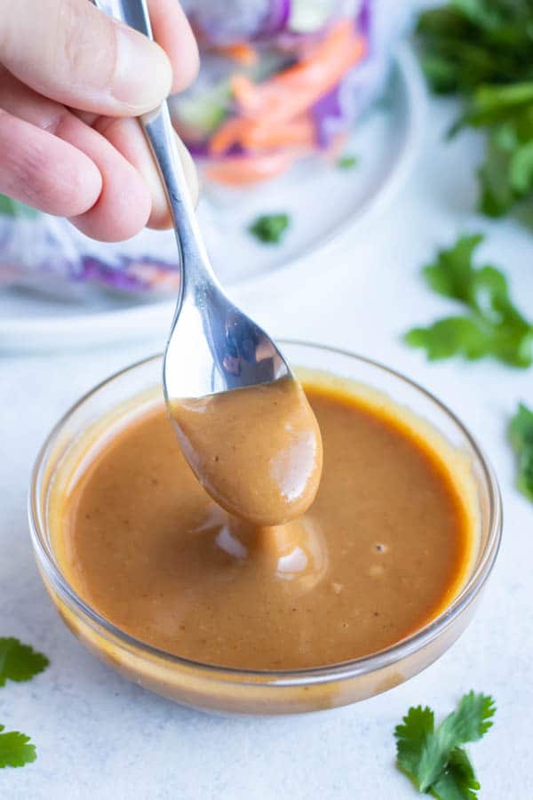 Peanut dipping sauce is dished with a spoon from a glass bowl.