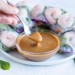 A spoon lifts up the peanut dipping sauce on a plate with spring rolls.