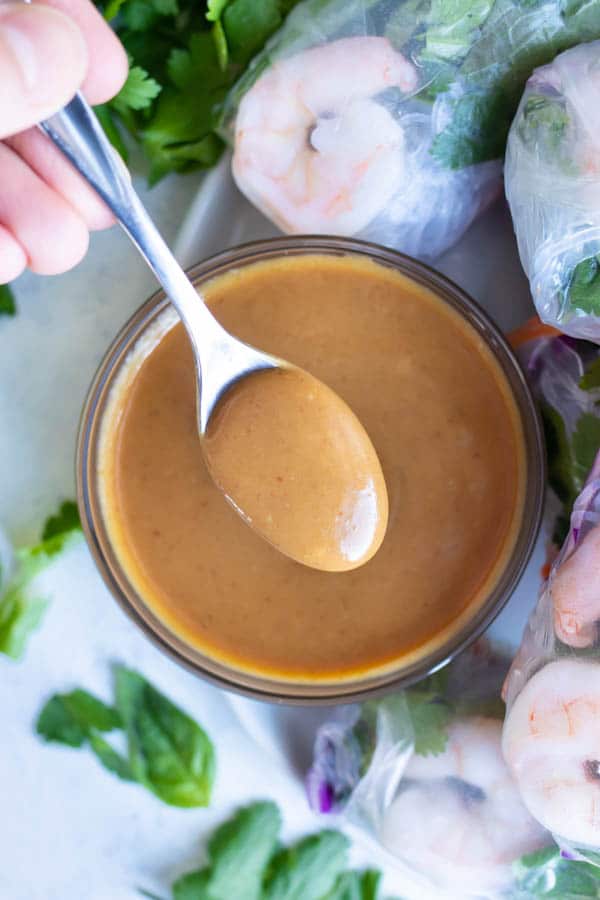 Thai peanut sauce is served with a spoon with fresh spring rolls.