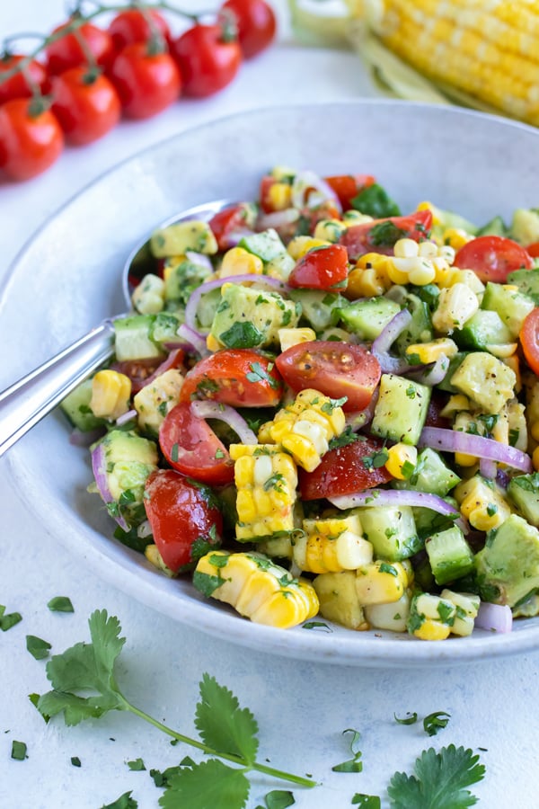 Avocado corn salad is served with a metal spoon from a white bowl.