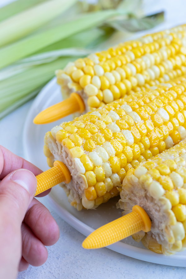 A hand is shown holding onto the plastic corn cob holders.