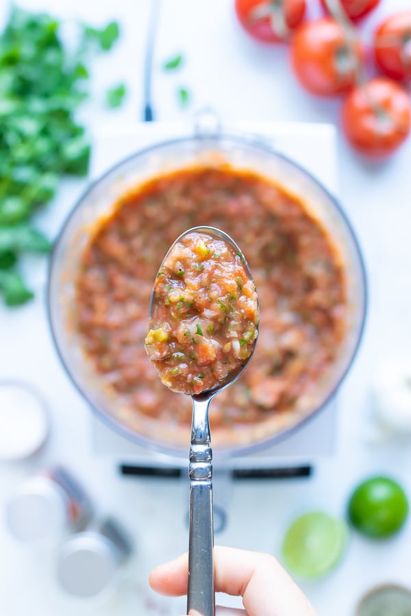 A metal spoon is used to lift healthy tomato salsa.