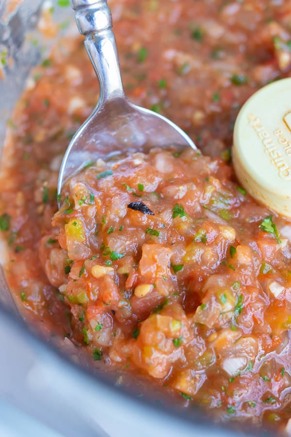Roasted tomato salsa is lifted from the food processor with a metal spoon