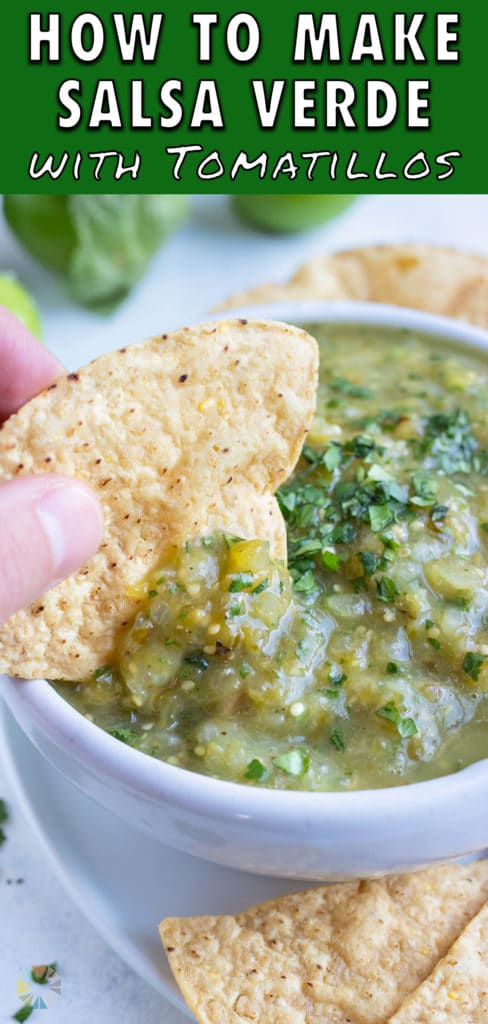 A hand is used to dip a tortilla chip into the bowl of salsa verde.
