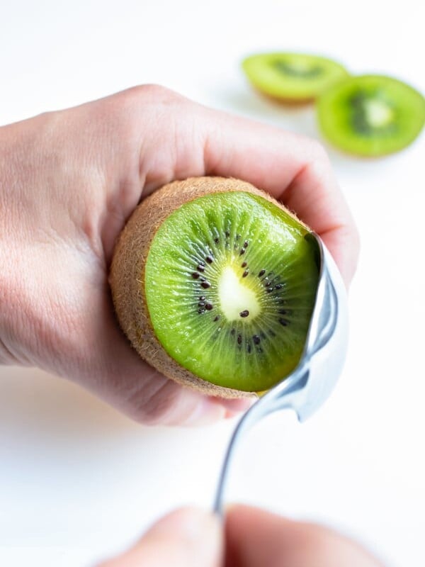 A kiwi is being cut and peeled by using the spoon method.