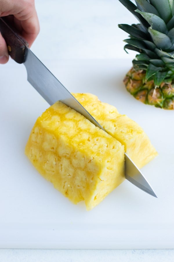 The half of the pineapple is laid on the counter and cut into quarters.