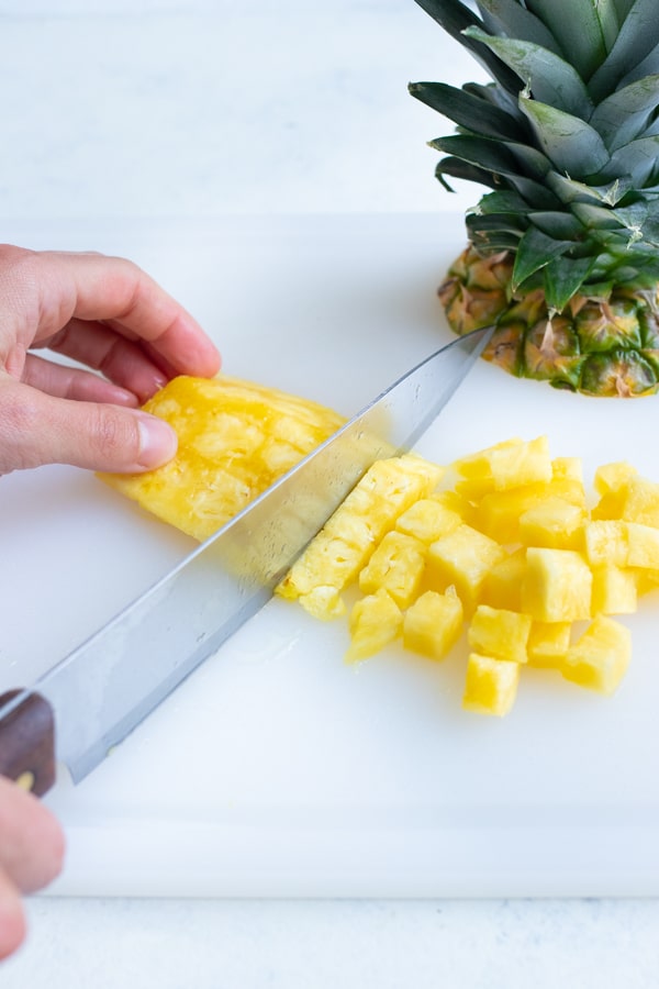 The pineapple quarter is cut into cubes with a knife.