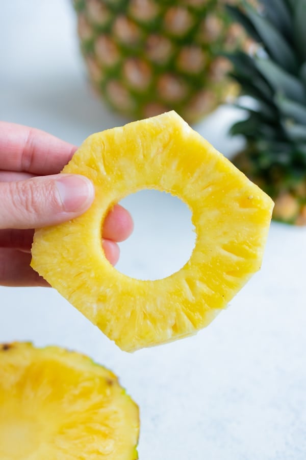 A hand is used to lift up a pineapple ring.