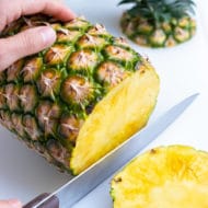 The bottom end of the pineapple is cut off with a large knife.
