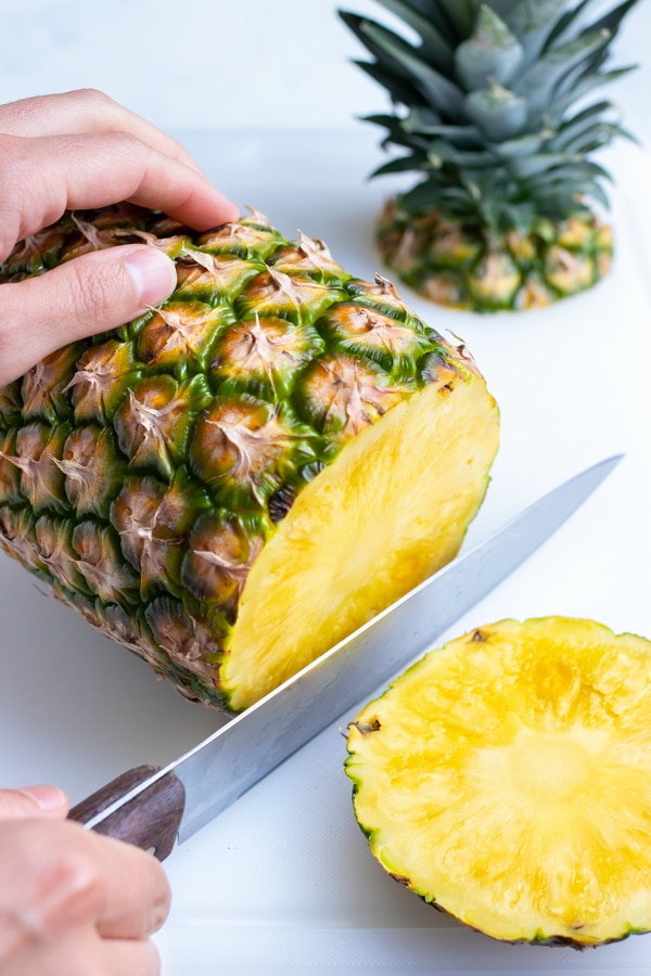 The bottom end of the pineapple is cut off with a large knife.