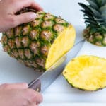 A knife is used to cut off the bottom of the pineapple.