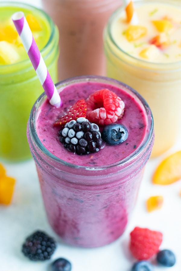 A berry smoothie is shown next to a kiwi and pineapple smoothie on the counter.