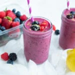 Two berry smoothies are set on the counter with ice.