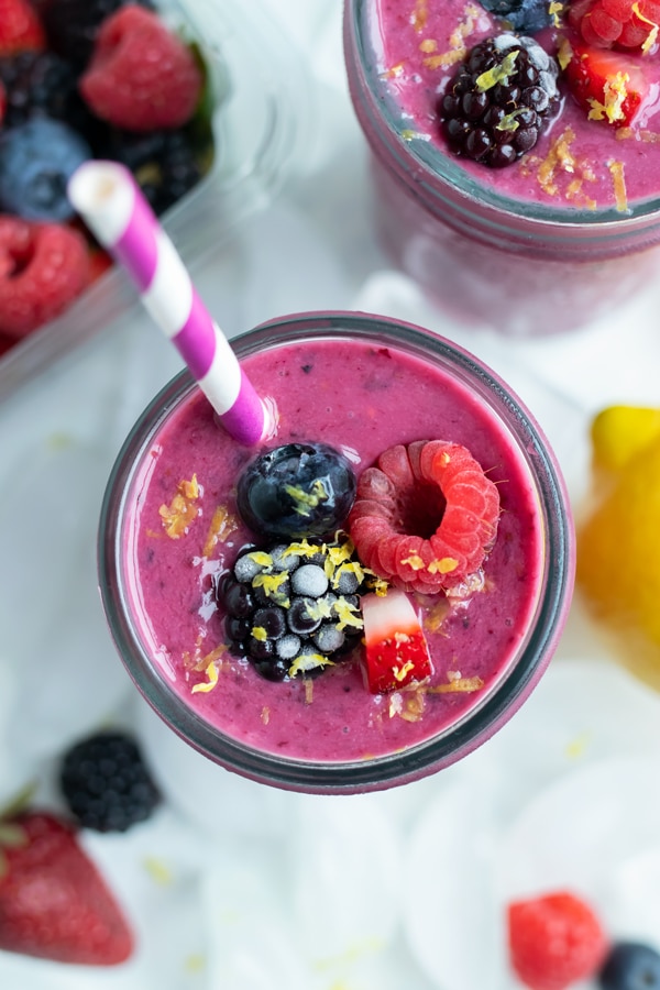 A berry smoothie is topped with frozen berries and fresh lemon zest.