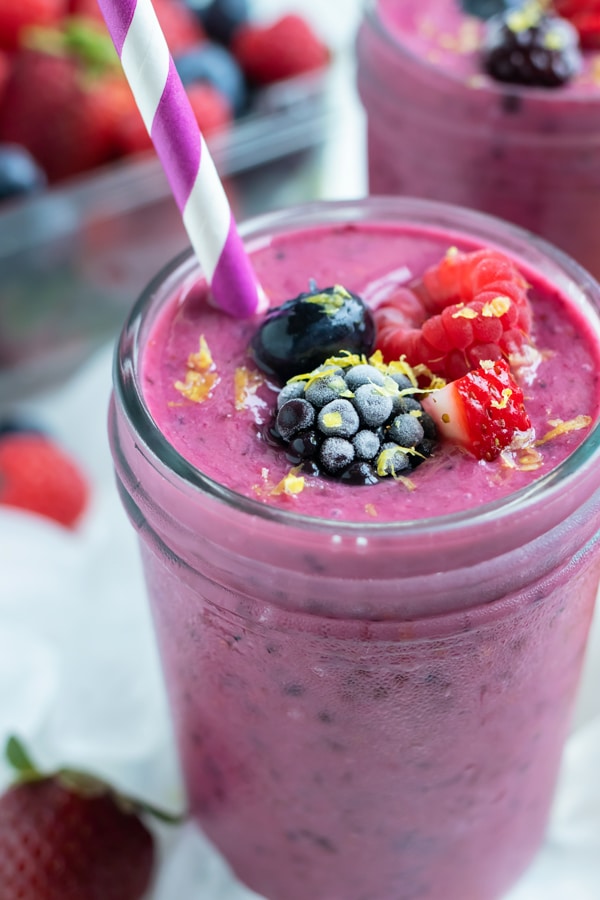 A thick berry smoothie is enjoyed for breakfast from a glass jar.