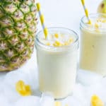 Pineapple smoothies are shown on the counter next to ice, bananas, and a whole pineapple.