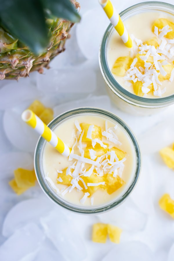 Creamy Pineapple and coconut smoothies are enjoyed with a straw from a mason jar.