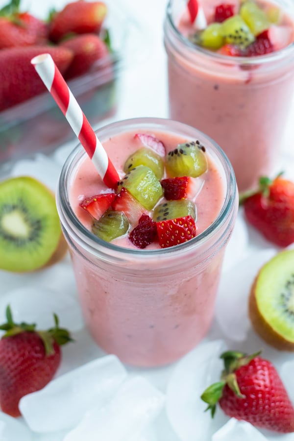 Two jars of strawberry kiwi smoothies are set on the counter.