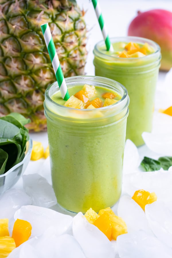 Healthy green smoothies are served on the counter next to a full pineapple.