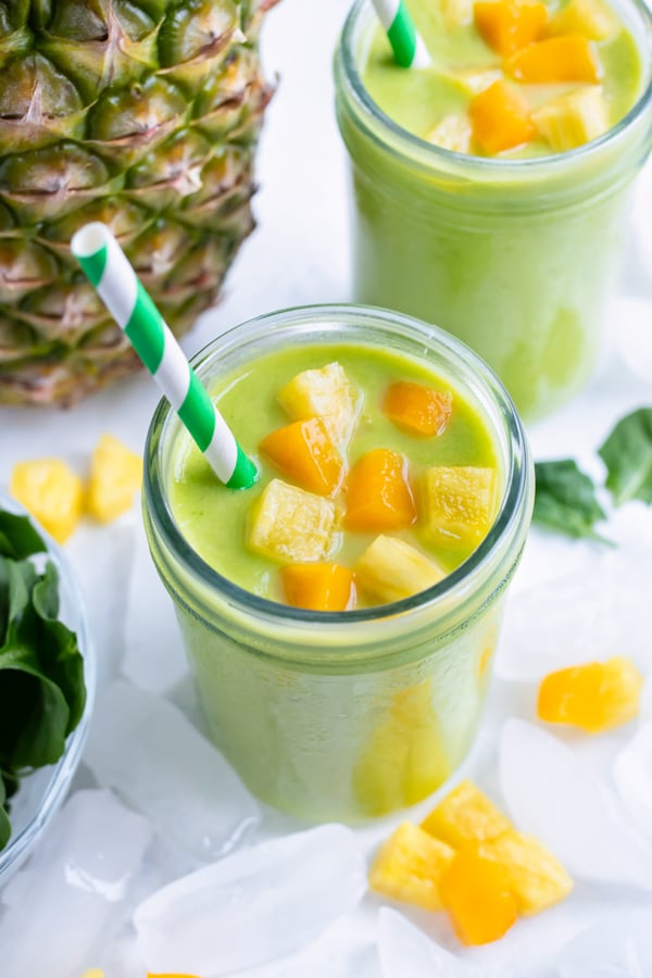 The two tropical green smoothies are topped with mango and pineapple chunks.