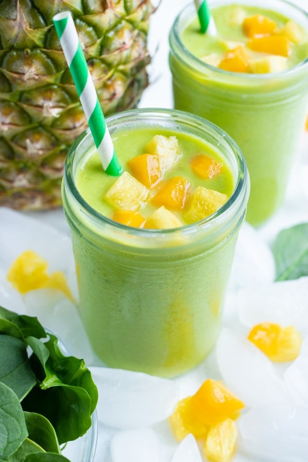 Two healthy green smoothies is set on the counter in a glass with a straw.