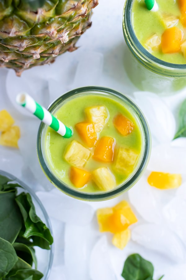 Smoothie topped with mango and pineapple is served with a straw next to pineapple.