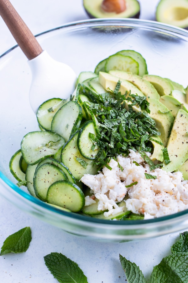 The cucumber crab avocado salad ingredients are combined with a spatula in a glass bowl.