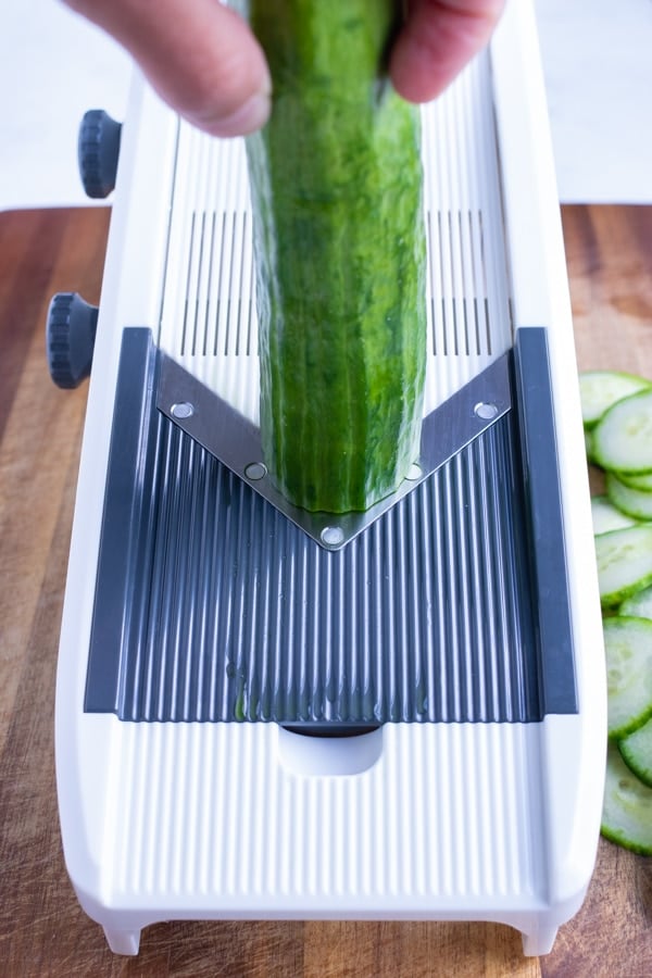 A cucumber is being sliced with a mandoline.