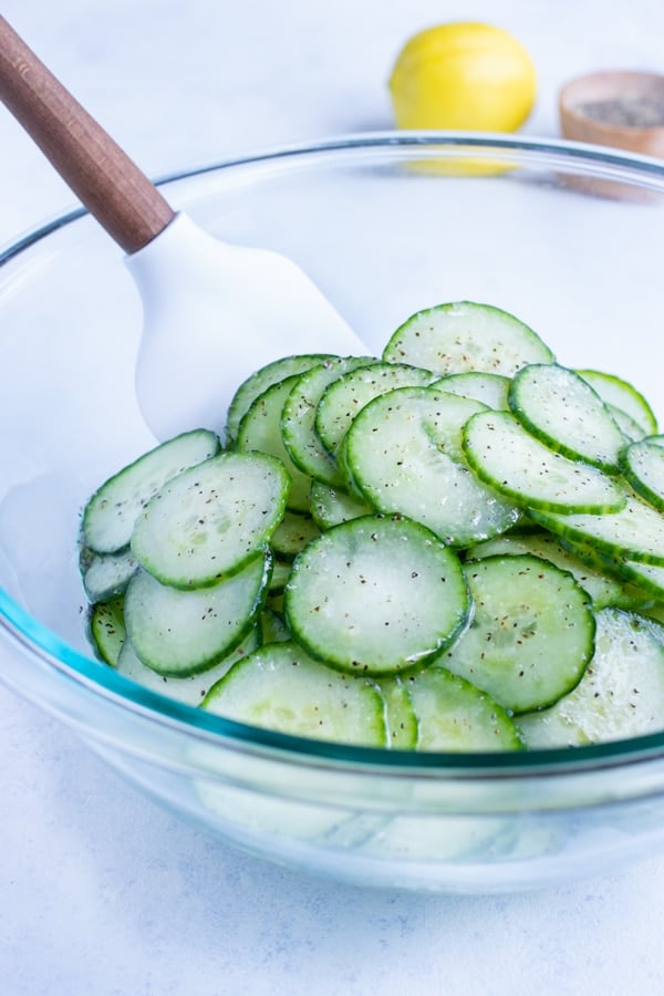 The lemon vinaigrette is combined with the cucumbers in a bowl.