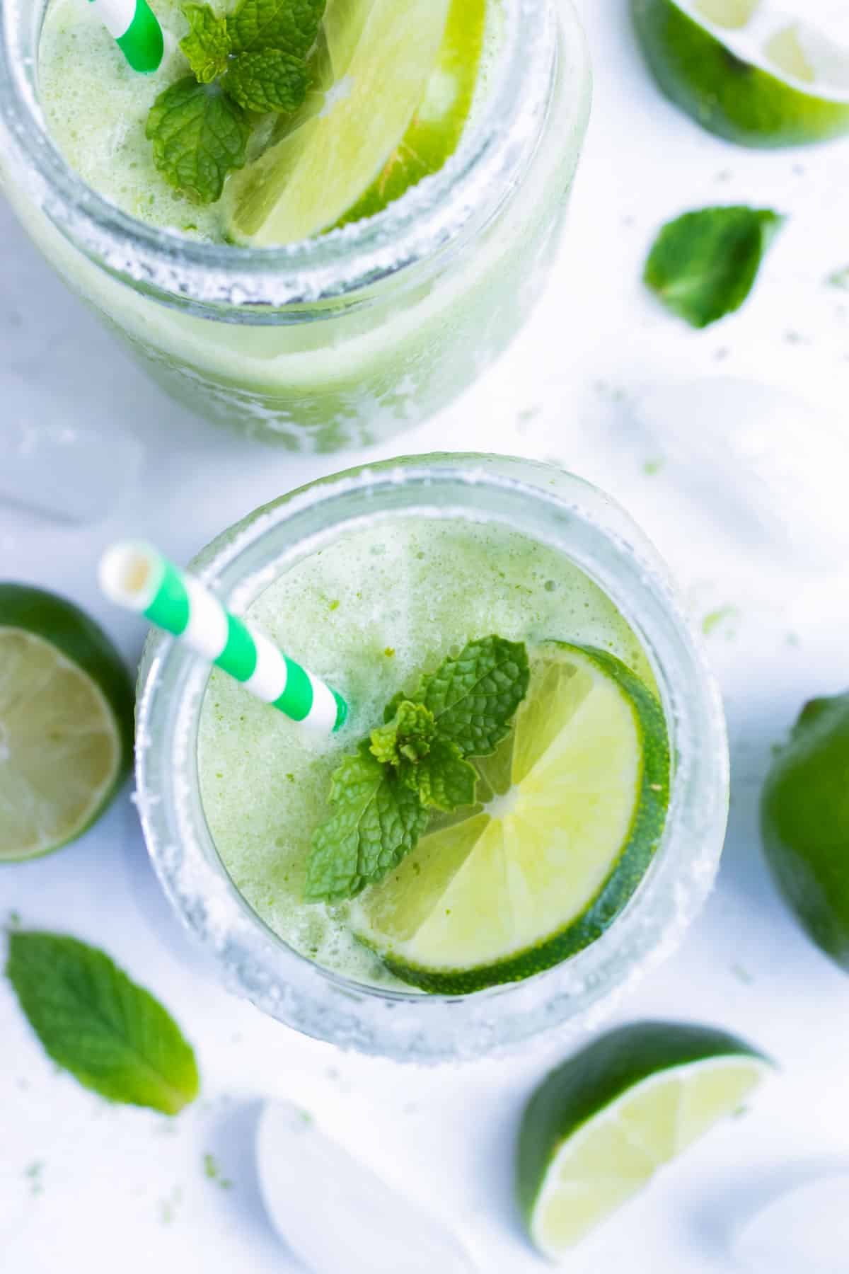 Two glasses of frozen mojito next to lime slices and mint.