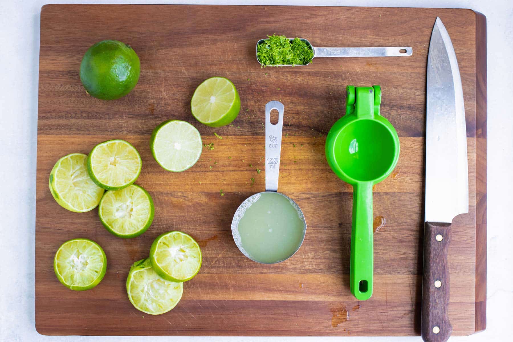 A cutting board with lime zest and a microplane and a citrus zester with fresh lime juice.