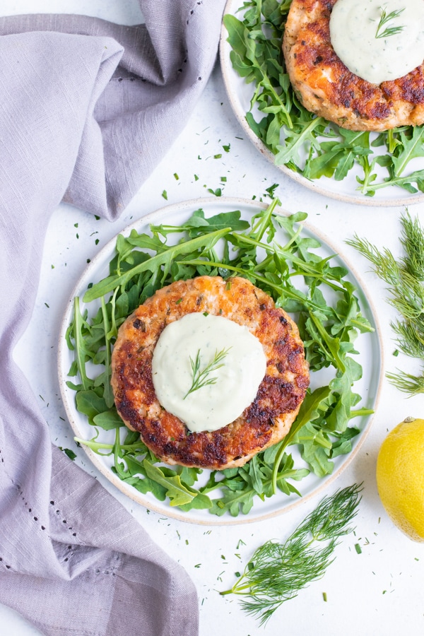 Homemade salmon burger is served on a plate of arugula..
