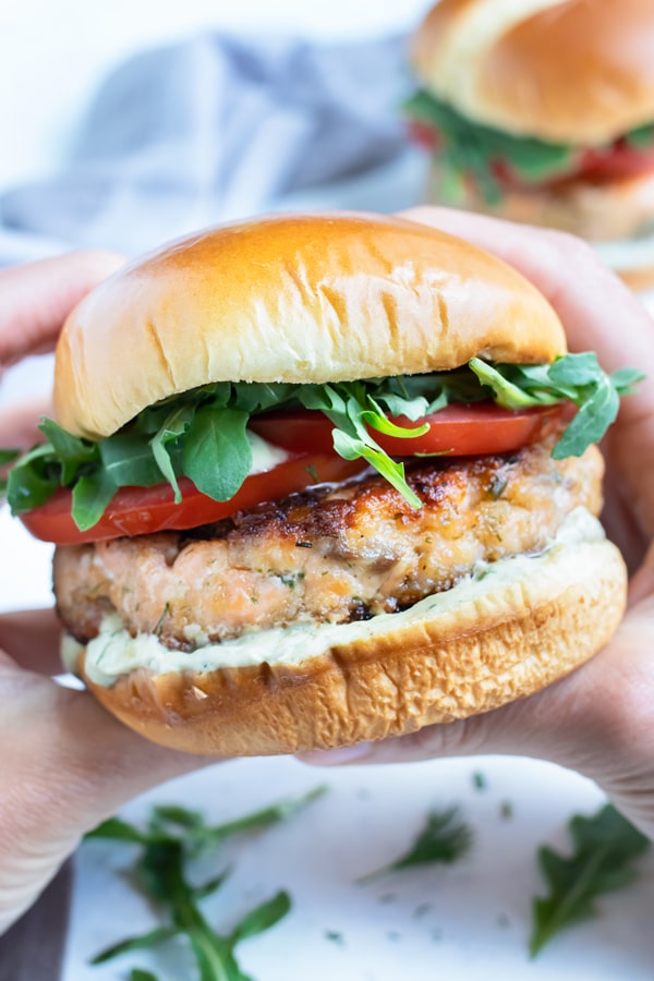 The salmon burger is held up by two hands.