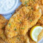 Crispy air fryer fish is served on a white plate with fresh lemon and tartar sauce.