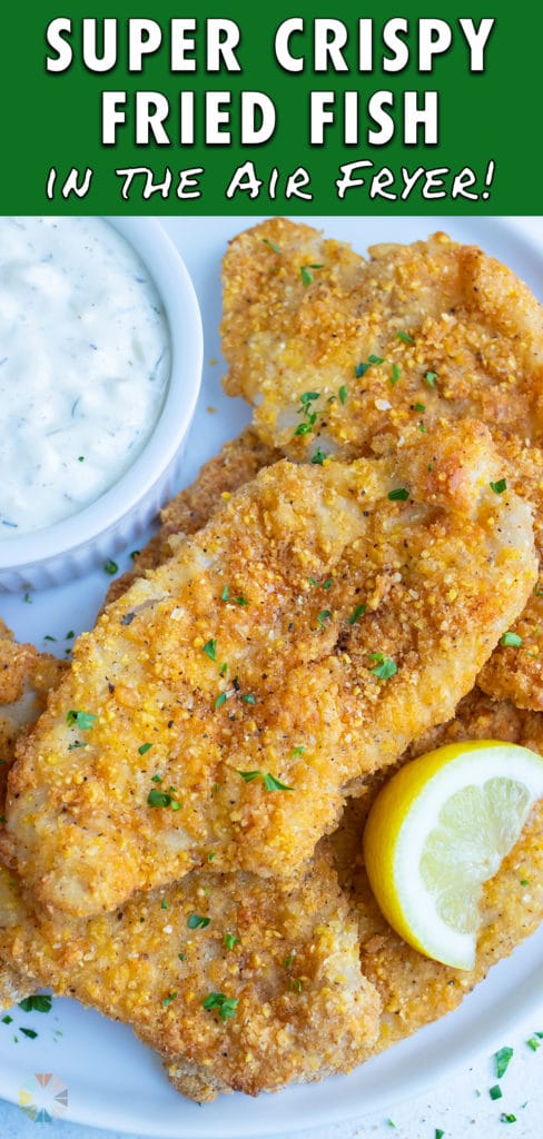 Crispy air fryer fish is served on a white plate with fresh lemon and tartar sauce.