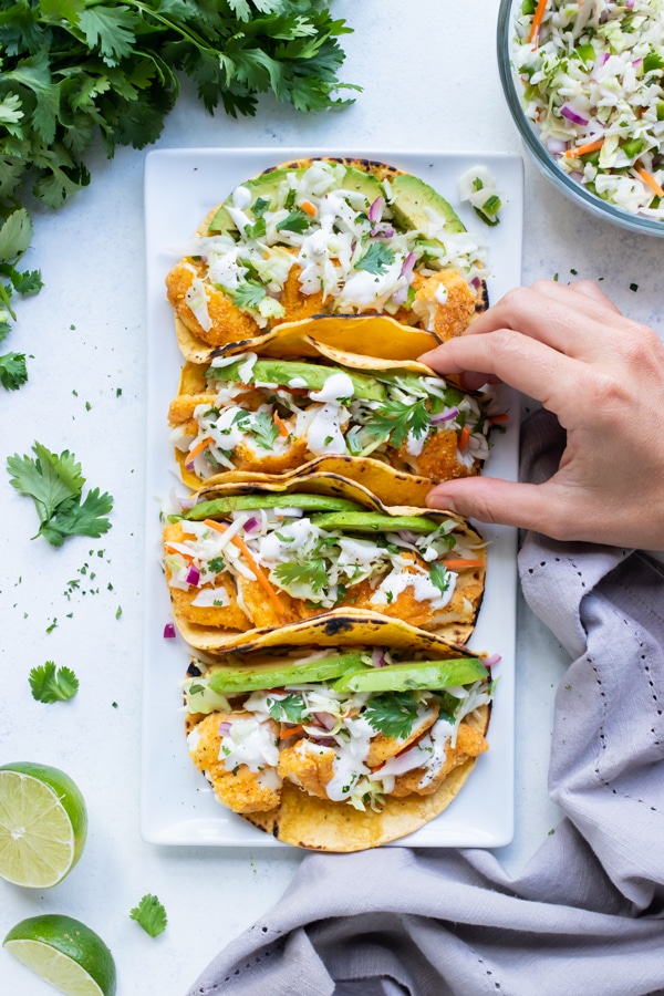 Tacos are lifted up by a hand from a white plate.
