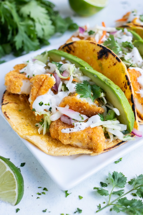 Loaded fish tacos are served on a white plate.