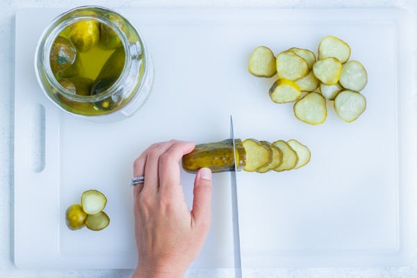 A dill pickle is sliced with a knife.