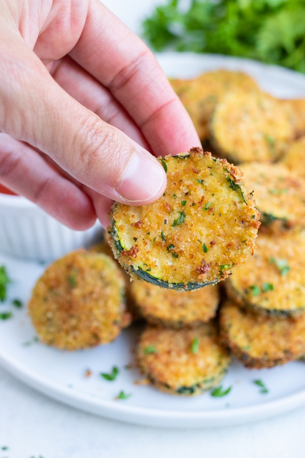 One zucchini chip is lifted up by a hand.