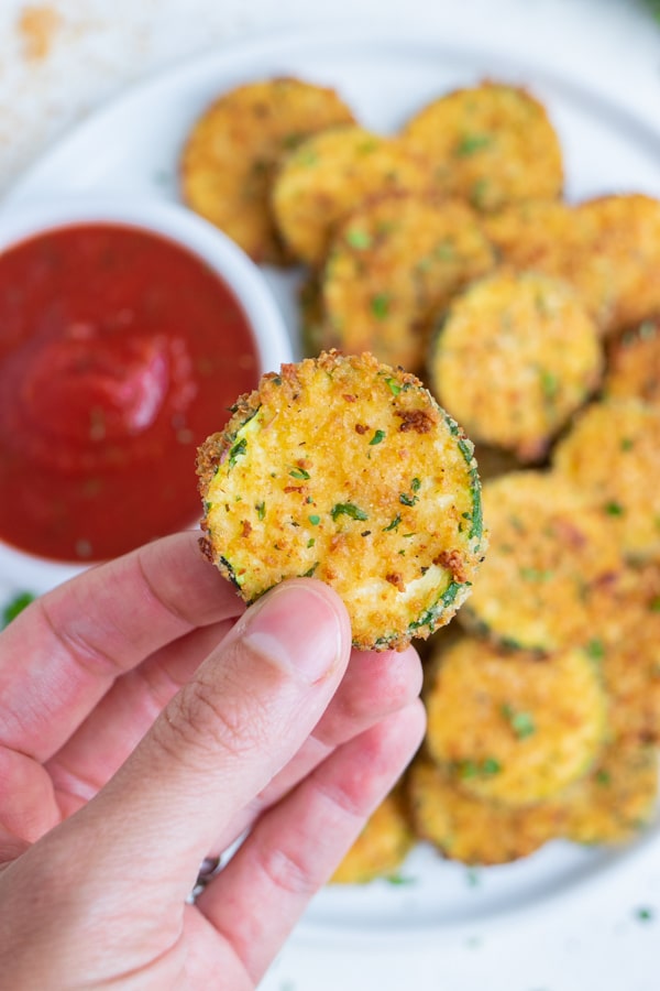 An air fryer zucchini chip is lifted up by a hand.